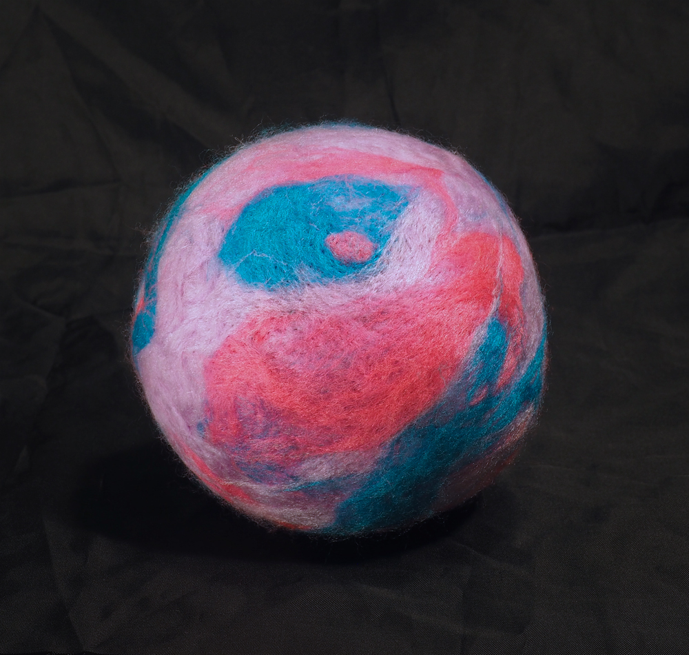 A ball-like doll with a needle felted surface. Swirls of blue, hot pink, and lavender give the spherical form a planetary appearance.