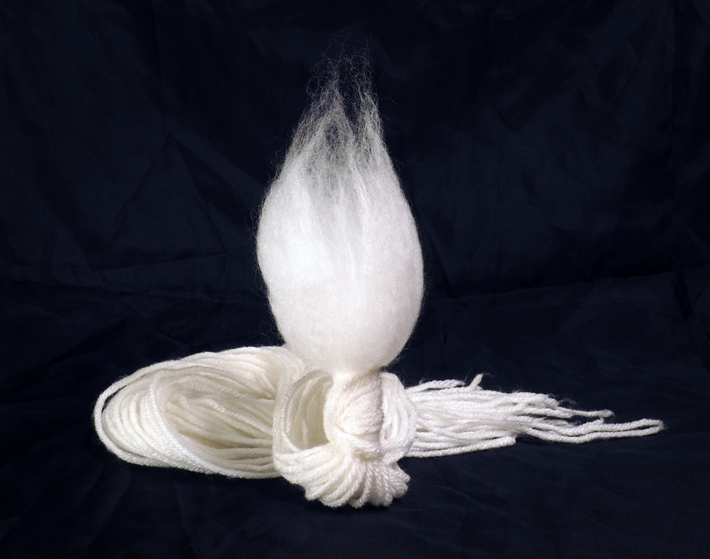 A yarn doll consisting of a long tail of loose white strands at one end, and a puff of brushed acrylic fiber at the other.